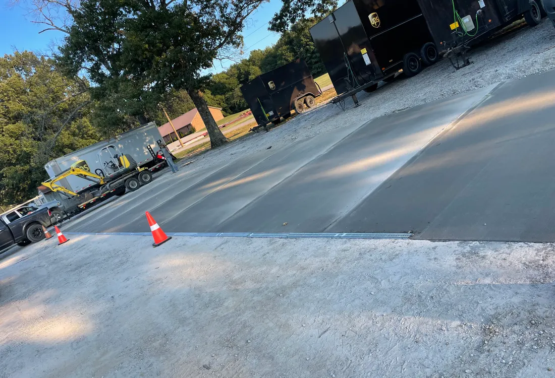 Fresh concrete lot section with traffic cones and paving equipment behind