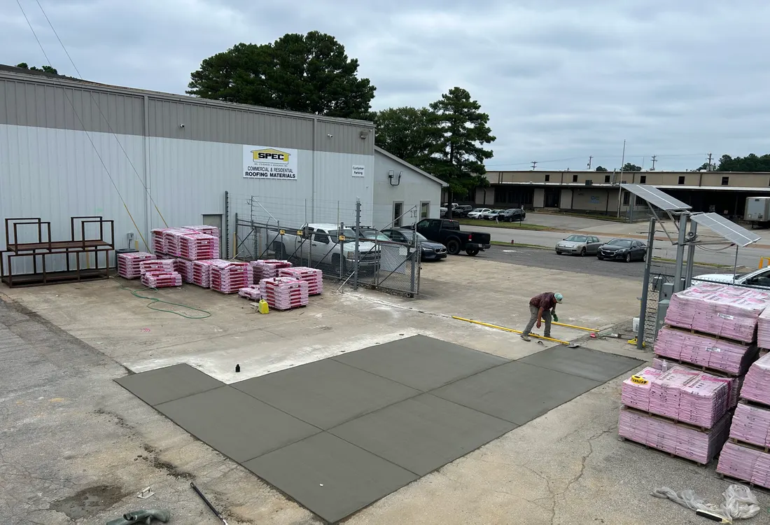 Finished concrete pad at a commercial yard with stacked materials behind