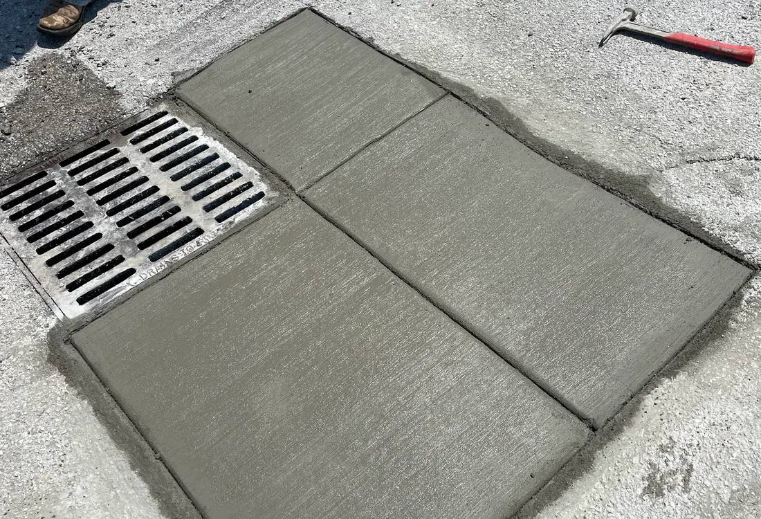 Fresh concrete patch tied in around a storm drain grate