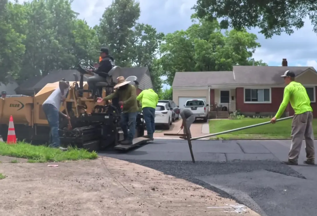 Paving crew working fresh asphalt behind the paver on a residential street