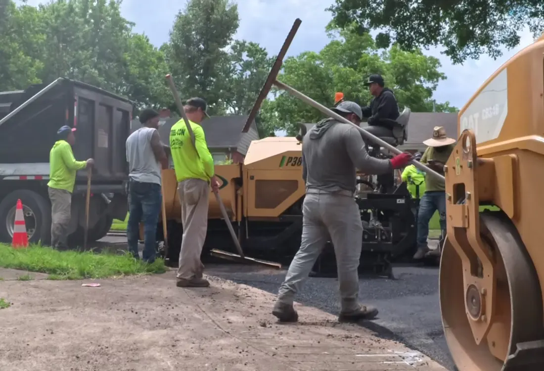 Roller compacting fresh asphalt with the crew and dump truck behind