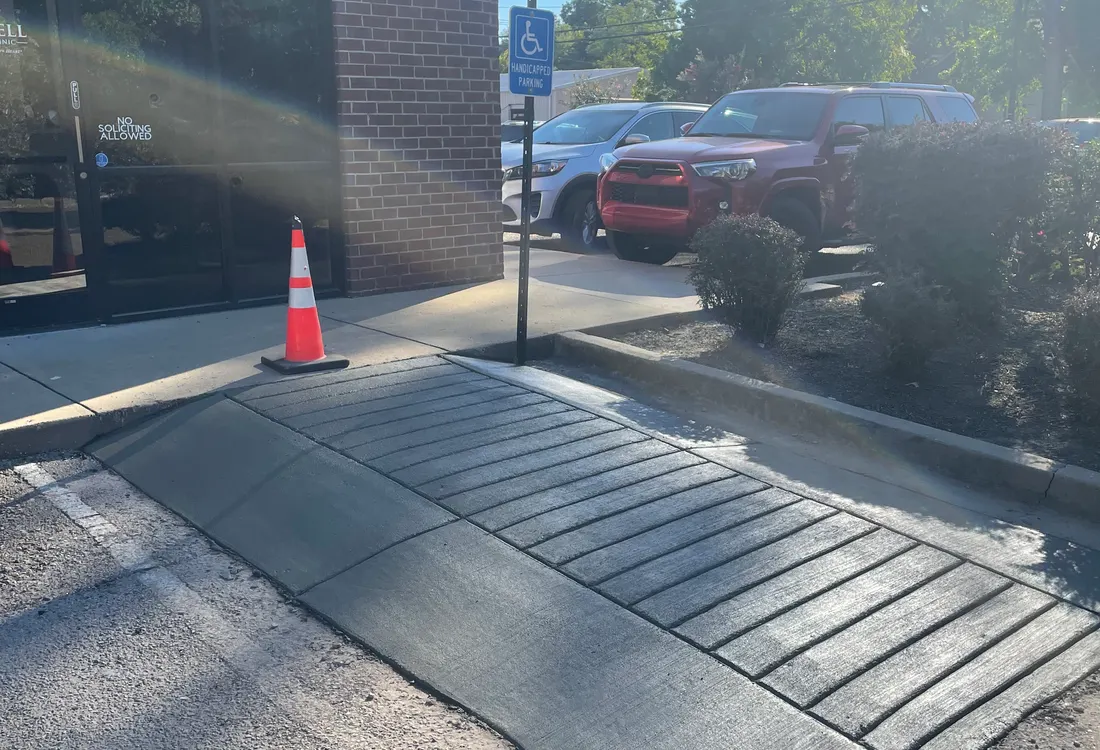 Grooved accessible ramp at a building entrance with a safety cone